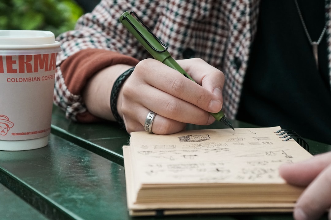 A hand drawing detailed sketches in a notebook beside a cup of coffee.