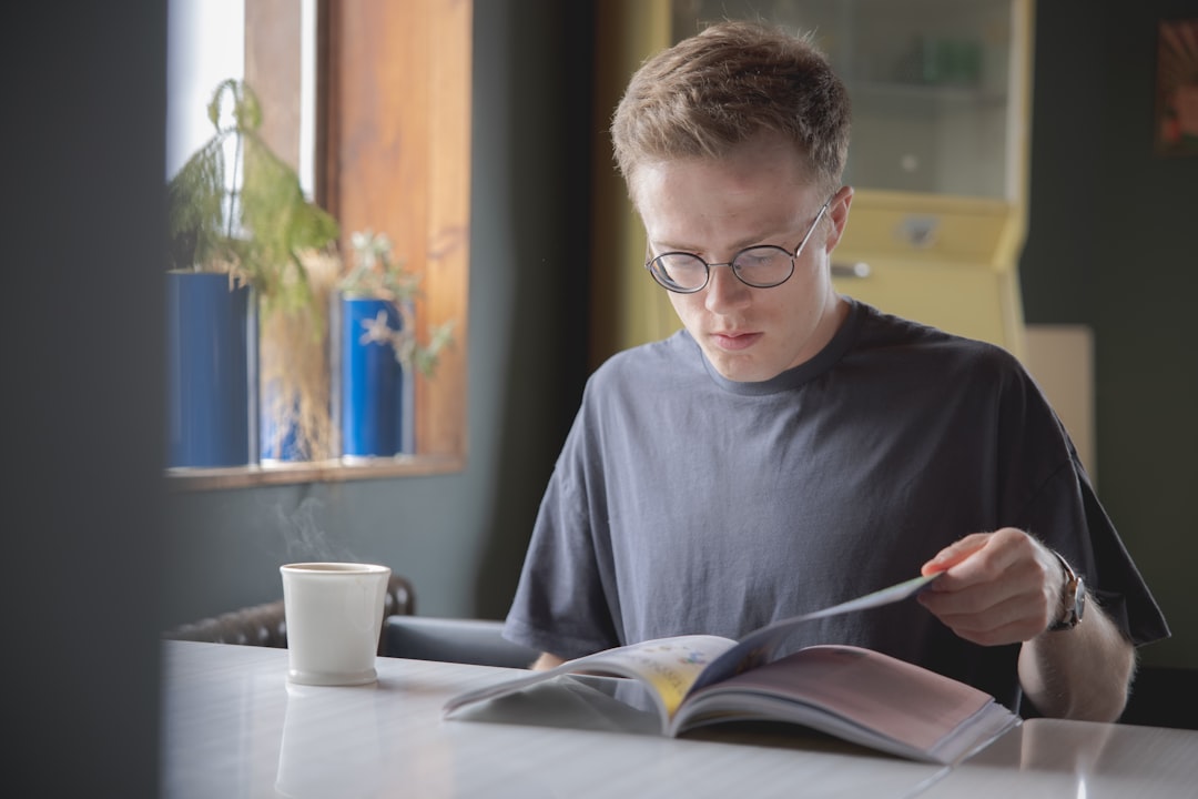 Teenage boy wearing glasses reading a book, representing a capable student who may appear disengaged at school