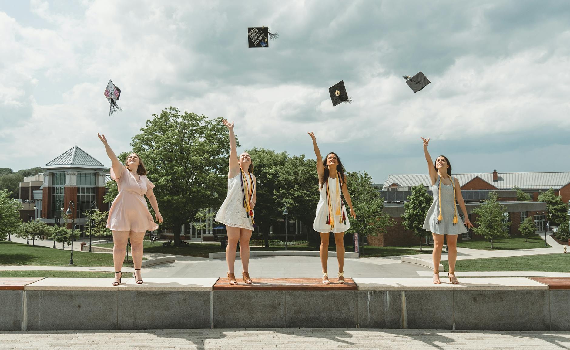 Four graduates joyfully tossing caps, celebrating the academic success this course helps achieve