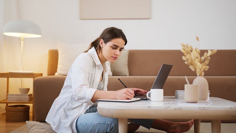 Young woman using laptop and taking notes during an online course